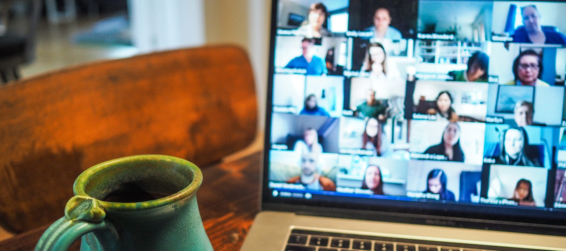 A mug near a laptop with a zoom meeting on the screen