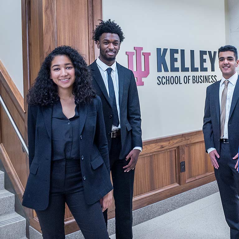 A group of Kelley School of Business undergraduate students stand in front of a wall that says Kelley School of Business.