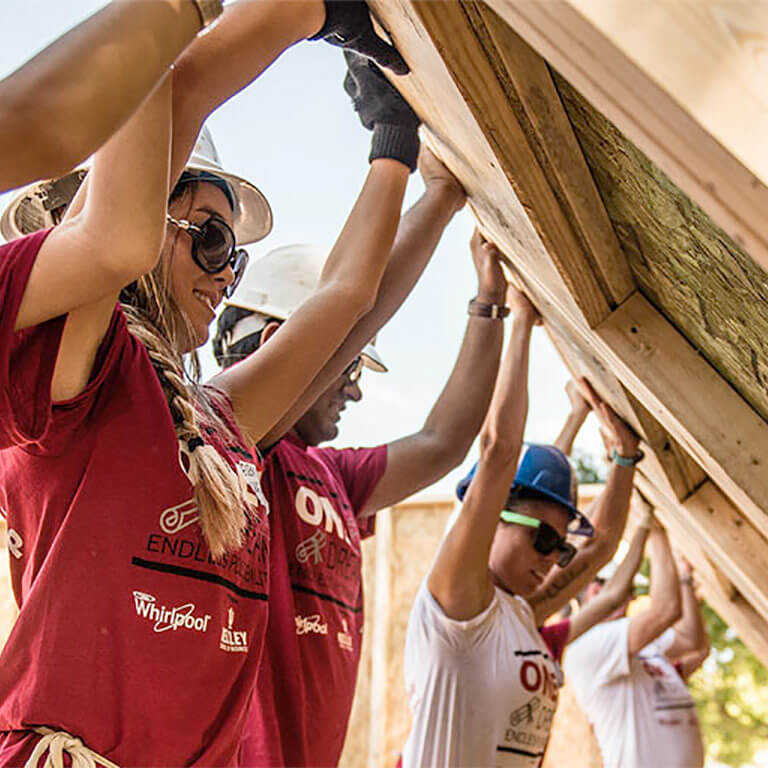 Kelley School of Business students are wearing hard hats and standing together to lift up a wall at the Habitat for Humanity Build event. 