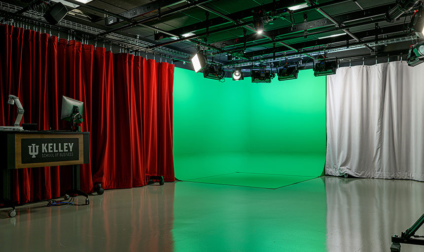 An empty studio filming room shows backdrop options including a red curtain backdrop, the green screen, and a white curtain backdrop. Lights and cameras are mounted in the ceiling.