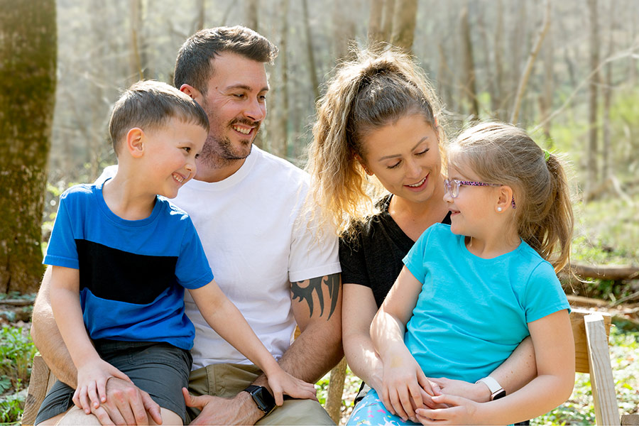 A family with a mother and father and two children are talking and smiling at each other during an outdoor hike.