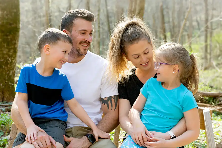 A family with a mother and father and two children are talking and smiling at each other during an outdoor hike.