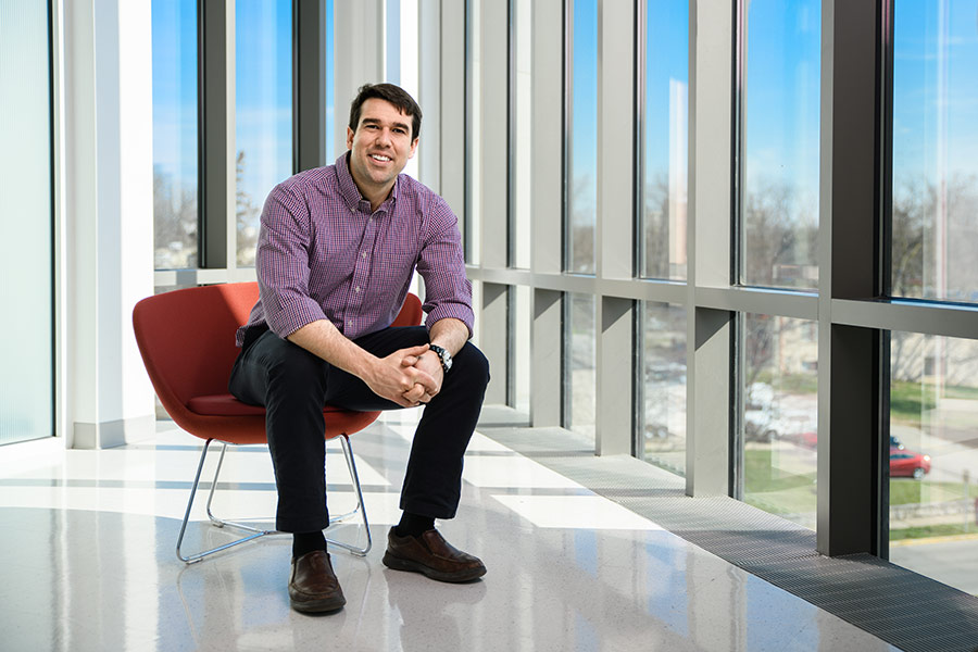 A graduate business student sits in a red chair against a wall of windows that overlook the Indiana University Bloomington campus.