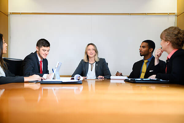 A group of MS in Finance students sit around a conference table in a team meeting with the executive director of the program.