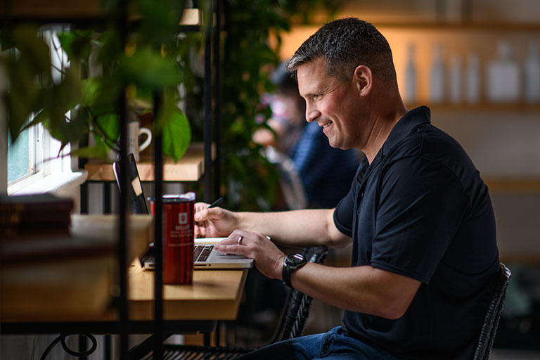 A Kelley Direct Online MBA student looks at a laptop while studying in a cafe. 