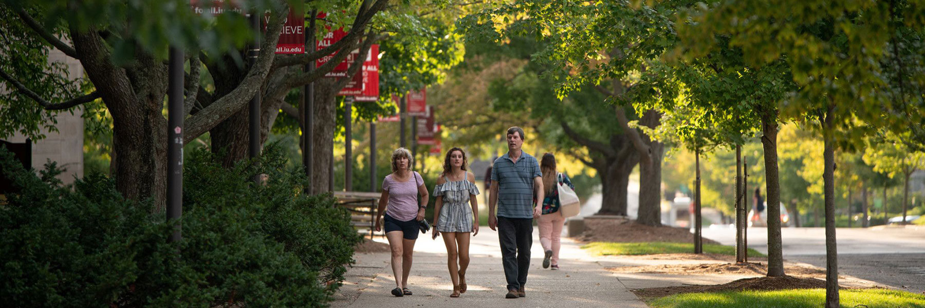 Three people walking on a tree-lined sidewalk on the Indiana University Bloomington campus during IU Family Weekend.
