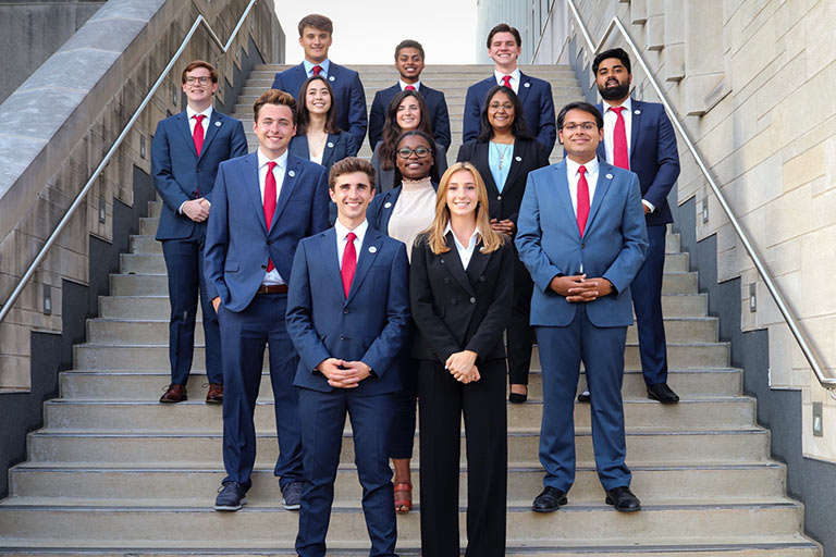 A mixed group of 13 students, who make up the executive committee for the Kelley Student Government, stand together on a flight of stairs outside.